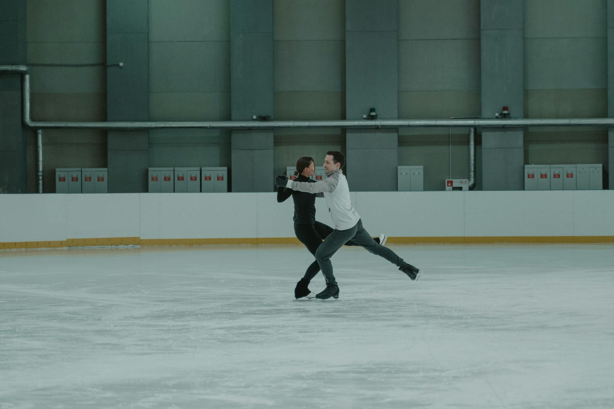 Two athletes gracefully perform a figure skating routine on an indoor rink.
